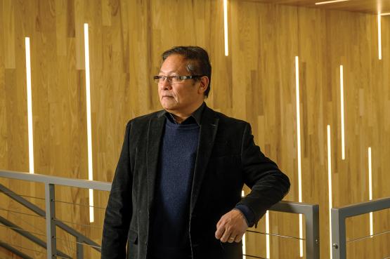  southeast Asian scientist Saw Wai Hla leans on a railing in front of a warm wood backdrop; he has dark hear and wears a black sport coat and glasses 