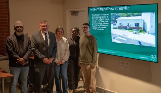  Voinovich School students and a member of the Mayors Partnership for Progress stand in front of a slide about the village of New Straitsville. 
