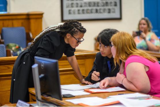  An instructor leans over a table to speak to two seated students 