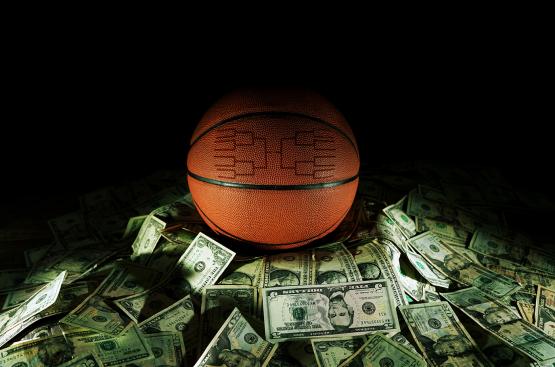  A basketball with a bracket engraved in it sits on a pile of U.S. currency. 