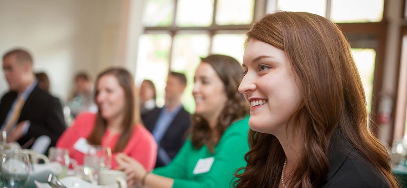 Woman smiles with others sitting at a table during a conference
