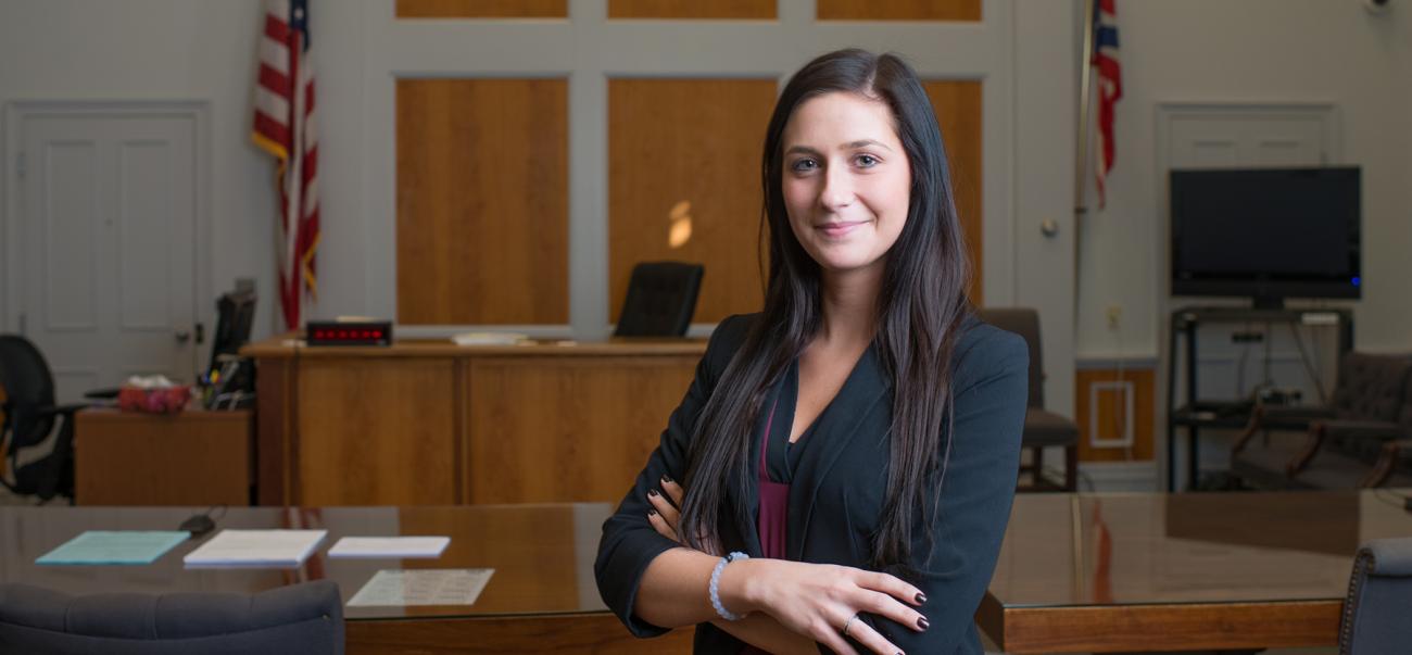 Pre-law student poses with her arms crossed in a courtroom.