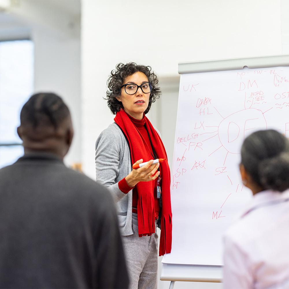 Woman in red scarf standing in front of whiteboard on easel