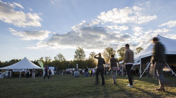 People walk around to different vendor tents at a festival during sunset