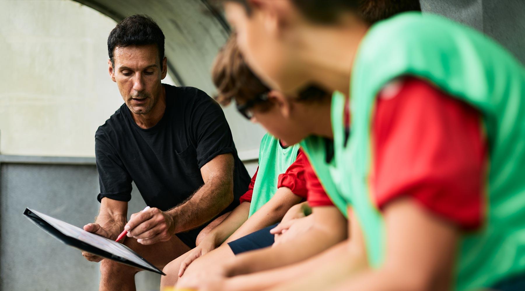 Man in black tshirt holding clipboard in front of boys in green jerseys