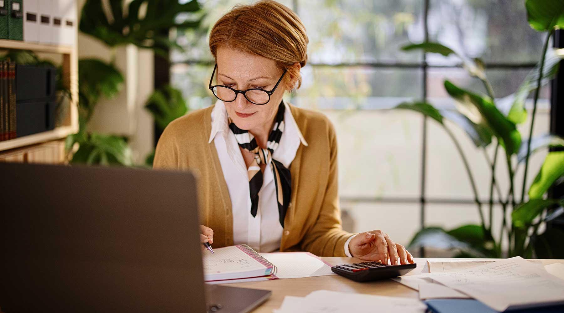 Woman at desk with open laptop using calculator