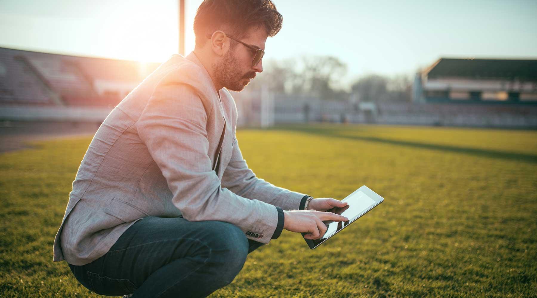 Sports manager on football field reviewing notes on his tablet