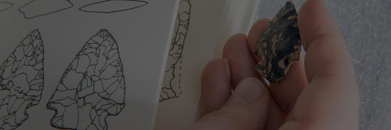 An Ohio University student holding an arrowhead and comparing it to reference material.