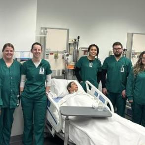 Nursing students surrounding a hospital bed with a mannequin lying in the bed as a patient