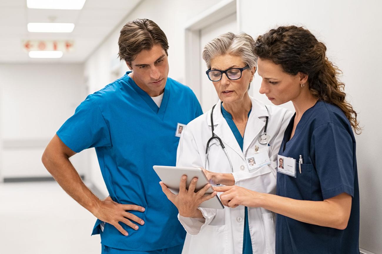 Three medical professionals standing in white hallway looking down at tablet one is holding
