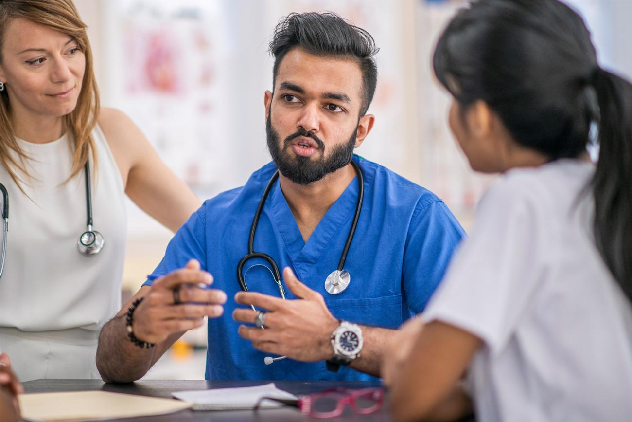 Man in bright blue scrubs sitting at table talking to women in white shirts