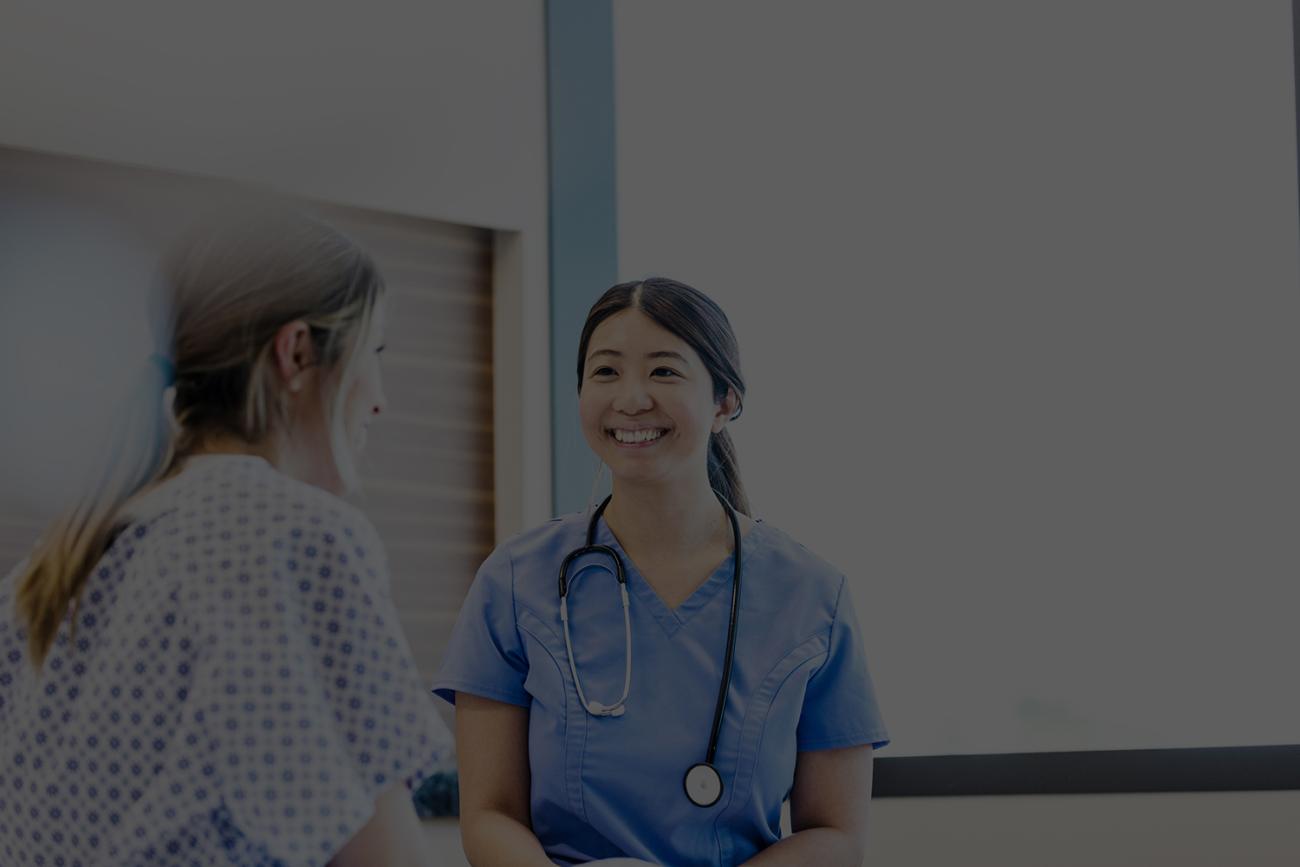 Woman in blue scrubs smiling at patient in hospital gown