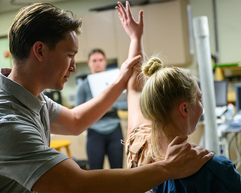 A student assistant assesses a patient's shoulder.