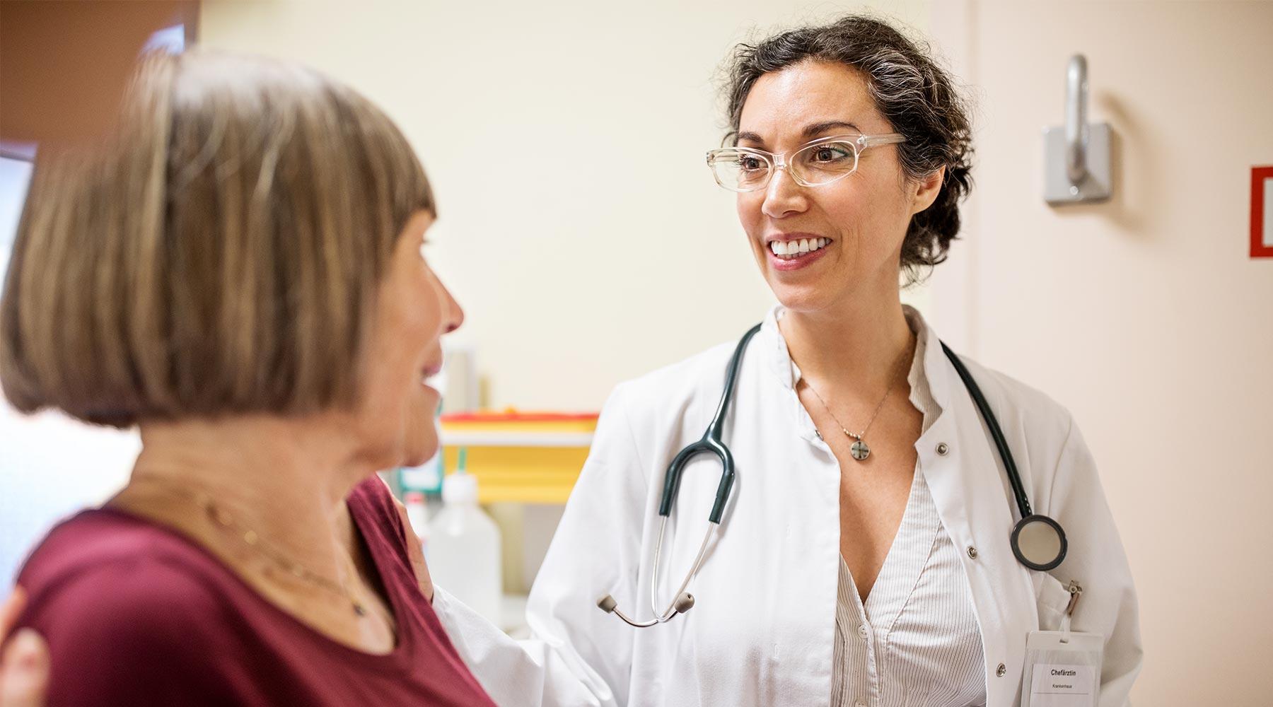 Female doctor with glasses and white jacket talking to a patient in maroon shirt