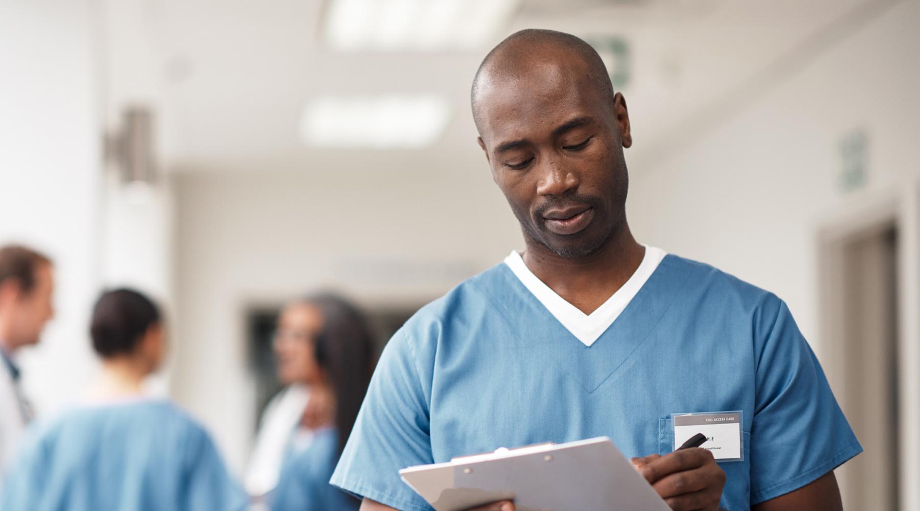 Bald African American man in blue scrubs writing on clipboard in his hand
