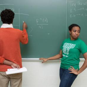 Teacher and a student at a chalkboard with equations 