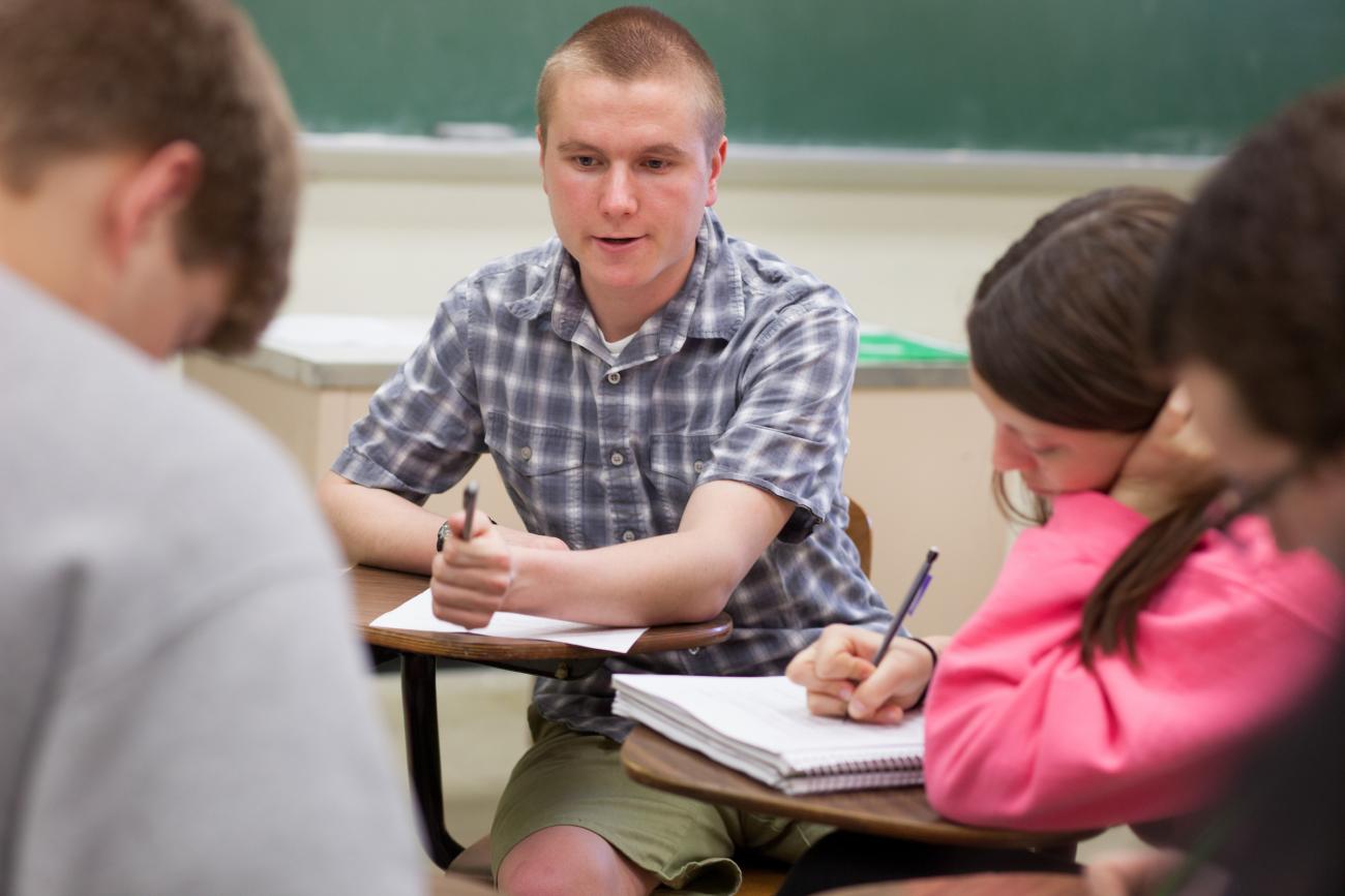 Teacher sitting at a desk talking with students