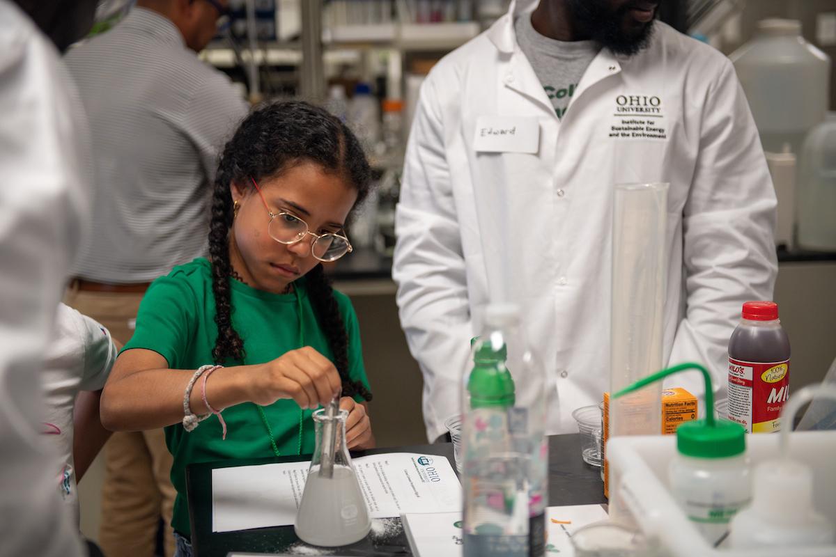 young girl using a beaker while an adult helps her expeirment