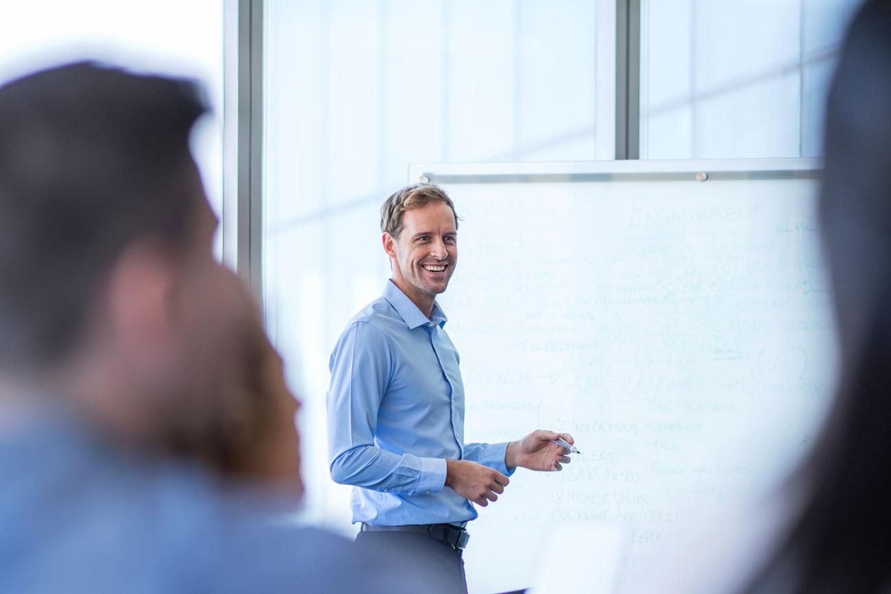 Engineering management professor in blue shirt standing in front of whiteboard
