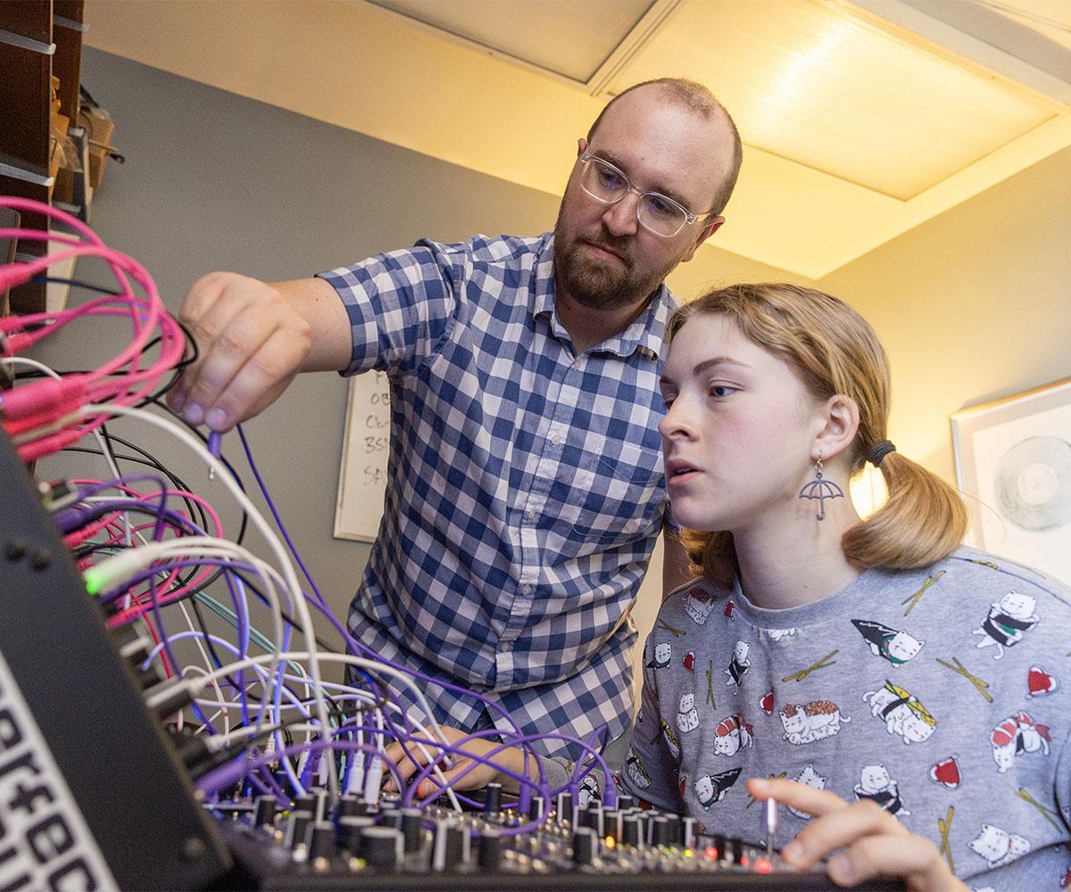 A professor works with a student who is composing music.