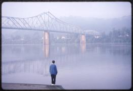 Woman in blue looking out over the misty Ohio River with the Ironton-Russell bridge visible in the distance
