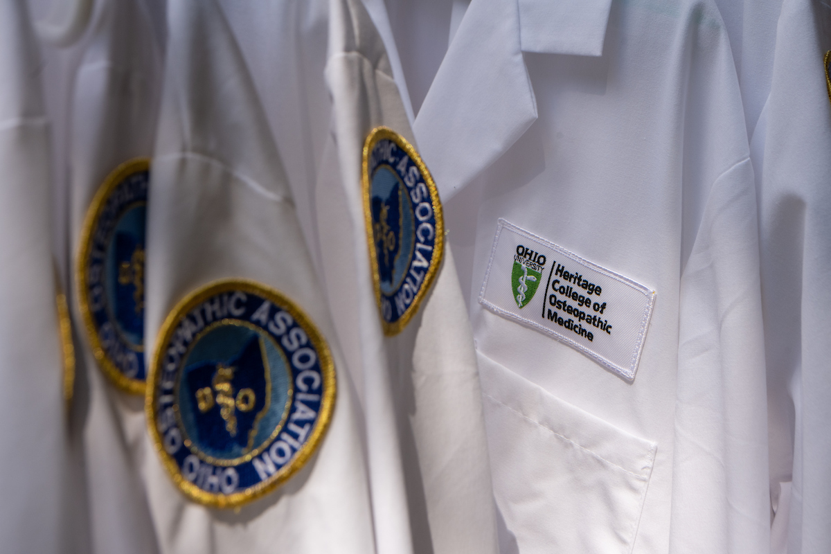 Multiple white coats with Heritage College logo on front and OOA patch on the arm