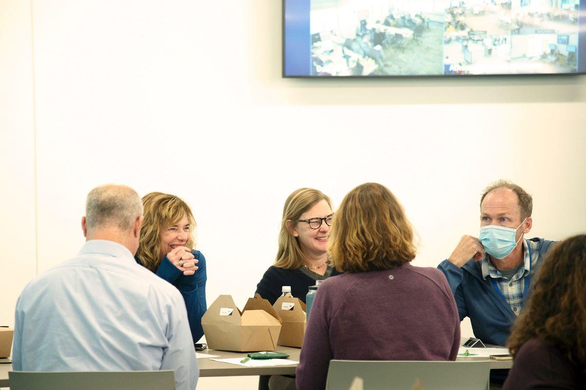 A group of Heritage College faculty sit around a table laughing