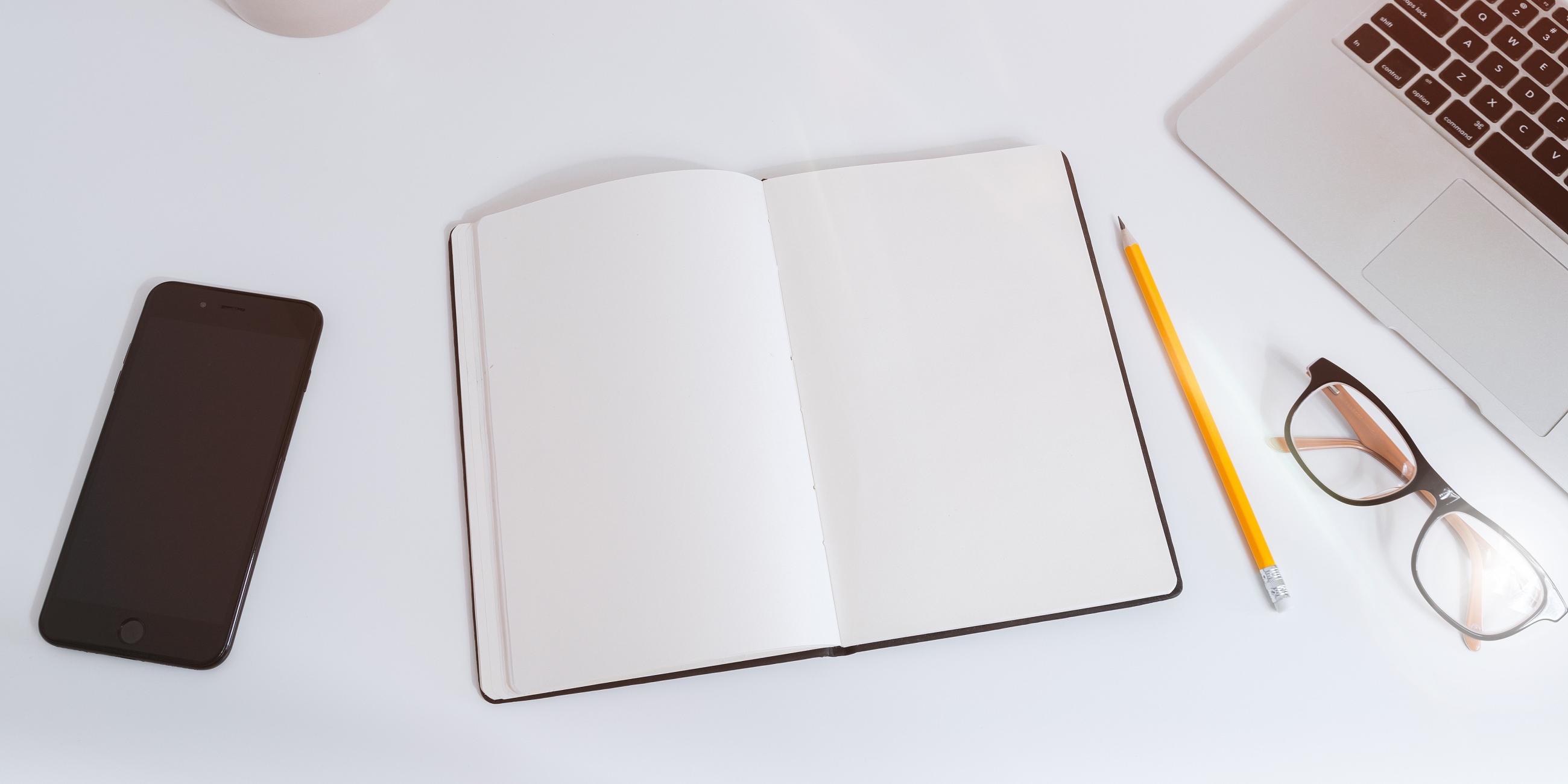 A phone, notebook, pencil, and glasses on a table