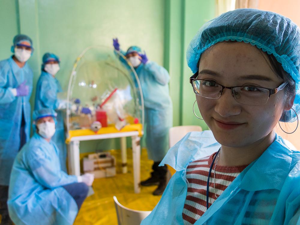 A student in lab gear smiles and 4 people pose in the background