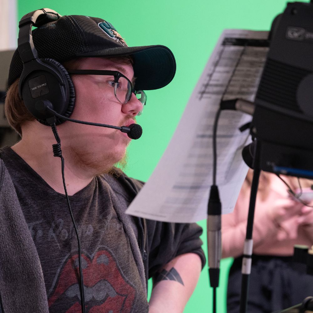 A man wearing a headset stands in front of a green screen