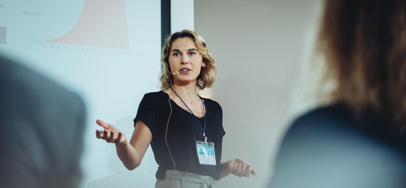 A woman speaks in front of a projector screen