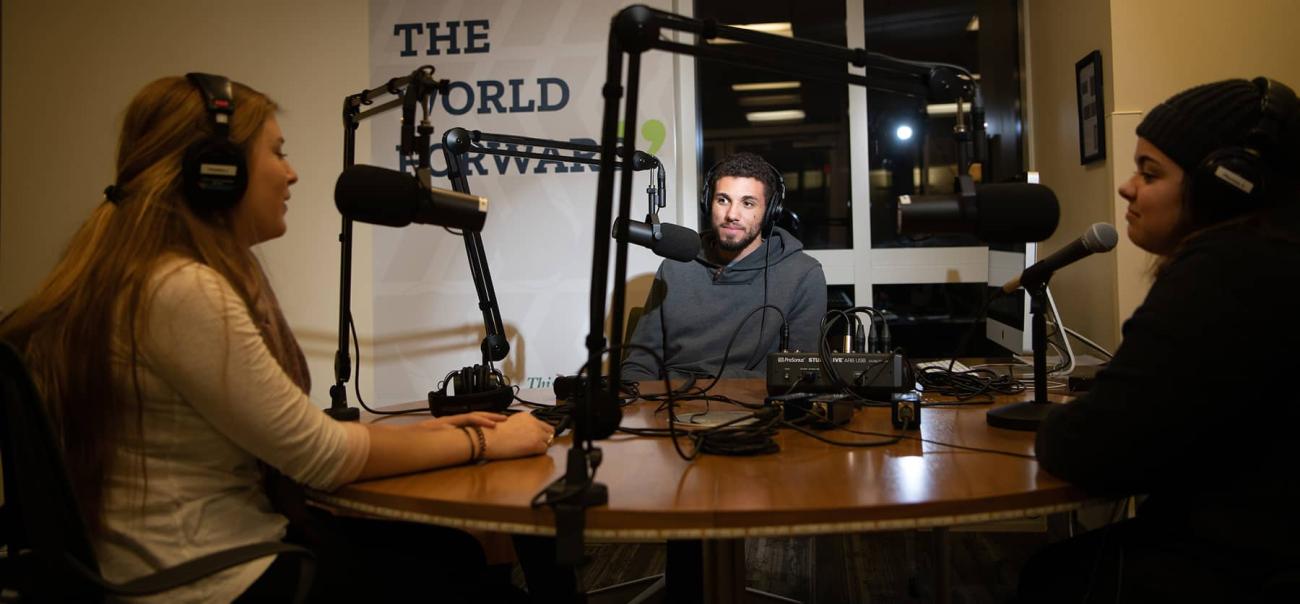 Three seated students actively using the podcast studio