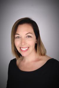 Jody Grove headshot, short brown hair, black shirt. grey background