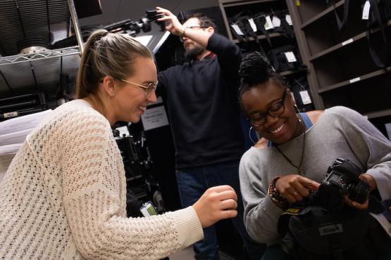 Two students look at a camera in the MDIA Equipment Room