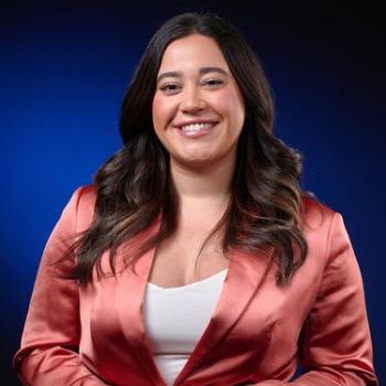 Chelsea Maldonado standing with hands across her chest, wearing a white shirt and shiny bright bronze blazer