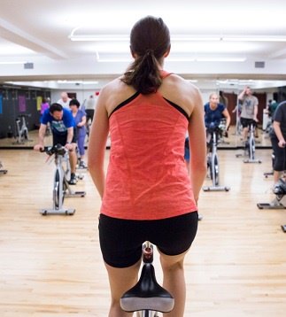 Group training instructor cycling on her bike in front of the class as they follow along on their stationary bikes.