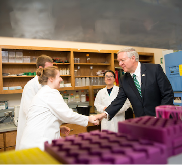 Scientists in laboratory greeted with handshake.