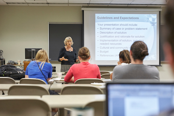 Classroom with one person standing and speaking and a small group of students listening