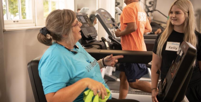 WellWorks member and personal trainer talking with another member on the treadmill behind them.