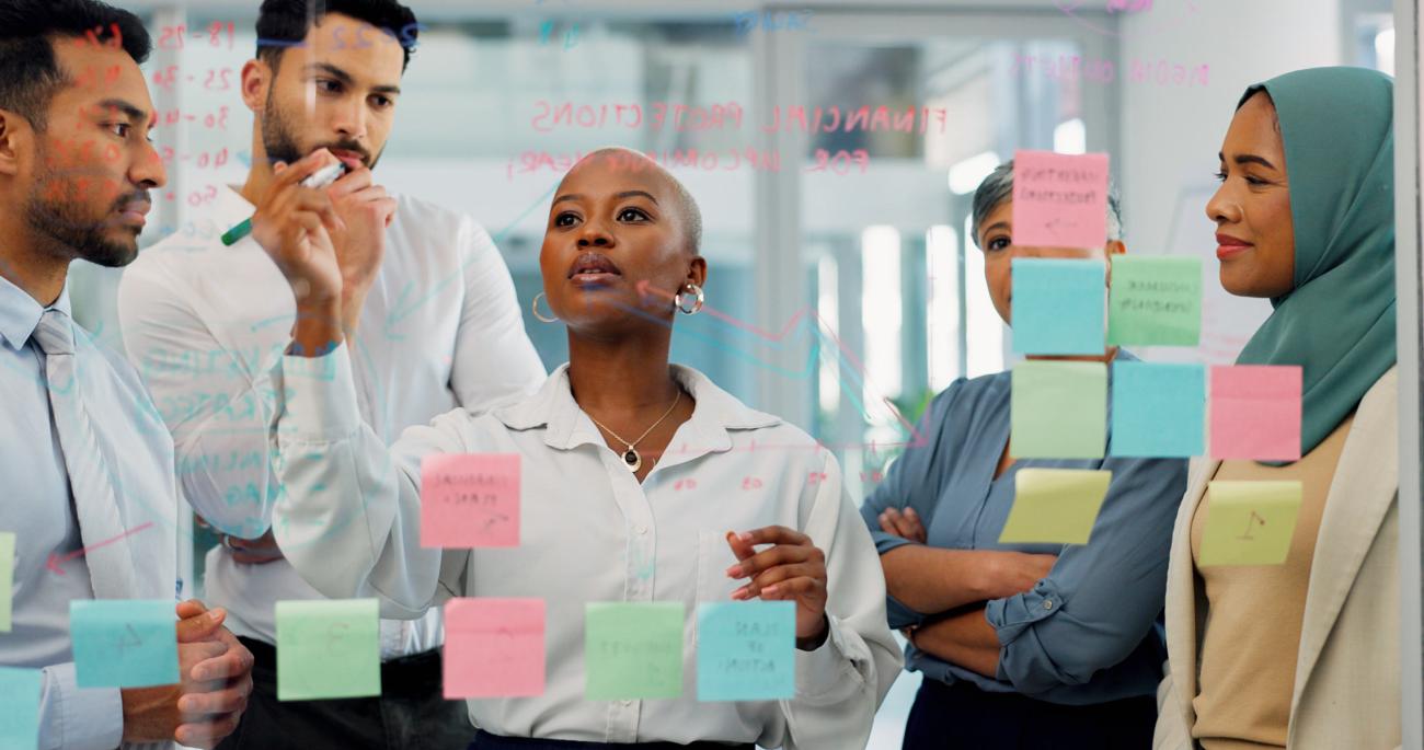 Business professionals meeting and writing notes on a board and using sticky notes to organize ideas