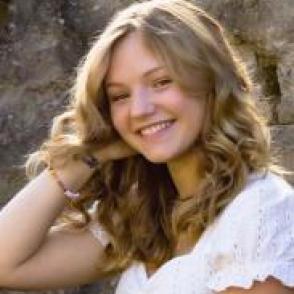 Abreanna Blose leans on her hand and smiles at the camera in a white blouse.
