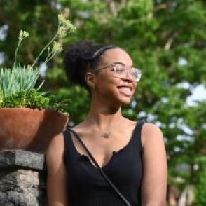 Alana Mitchell looking off to the side in a black tank top with plants in the background.