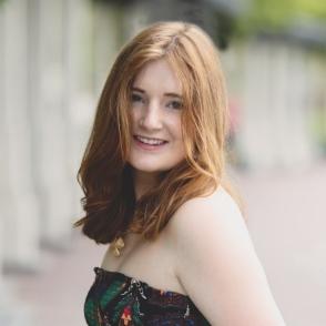 An image of Alyssa Gray in a paisley-patterned dress, holding a pink flower.