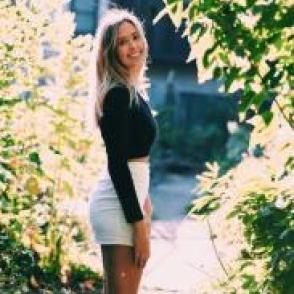 Beret Traum stands in the sun, wearing a long sleeve black shirt and a white skirt.