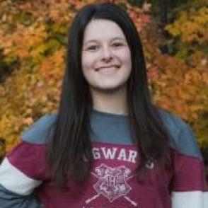 Carlene Edmonds smiling with one hand on her hip, wearing a striped shirt that says 'Hogwarts Alumni.'
