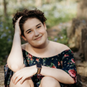 Claire Shelpman sitting down, leaning her head on one hand while wearing a black floral blouse.