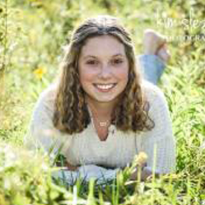 Emerson Wolfe laying in a green field in a white sweater and blue jeans.