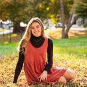 Emily Arnold sitting in autumn leaves in an orange dress with a black sweater underneath.
