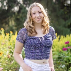 Emily Keith in a floral dark blue shirt and white pants with a flower field in the background.