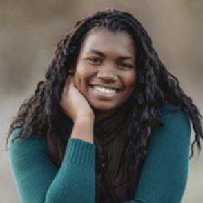 Emmarald Jean-Francois leans forward on one hand, wearing a green-blue sweater and smiling.